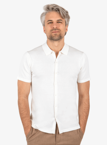 Man wearing white knit button shirt, standing with hands in pockets and facing forward.